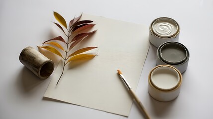 Artistic flat lay featuring dried leaves paint pots and art supplies on a white background