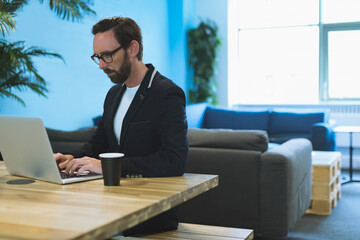 Laptop sitting on wooden table in office lounge with black paper coffee cup and potted plants © wavebreak3