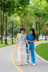 Asian nurse assists elderly woman who walks with a cane. Assists and cares for elderly female patient who is doing physical therapy in a park.