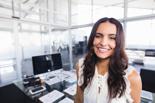 Female professional standing beside desk in open-plan office smiling and using computer keyboard