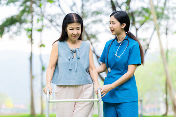 Asian nurse assists elderly woman who walks with a cane. Assists and cares for elderly female patient who is doing physical therapy in a park.