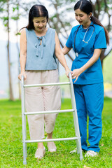 Asian nurse assists elderly woman who walks with a cane. Assists and cares for elderly female patient who is doing physical therapy in a park.