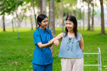 Asian nurse assists elderly woman who walks with a cane. Assists and cares for elderly female patient who is doing physical therapy in a park.