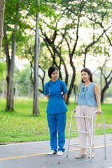 Asian nurse assists elderly woman who walks with a cane. Assists and cares for elderly female patient who is doing physical therapy in a park.