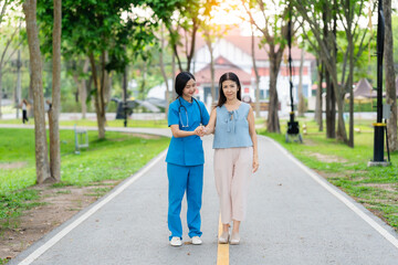 Asian female doctor takes care of elderly female patient in the park, helps the patient walk and exercises her legs and knees in the park.