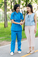 Asian female doctor takes care of elderly female patient in the park, helps the patient walk and exercises her legs and knees in the park.