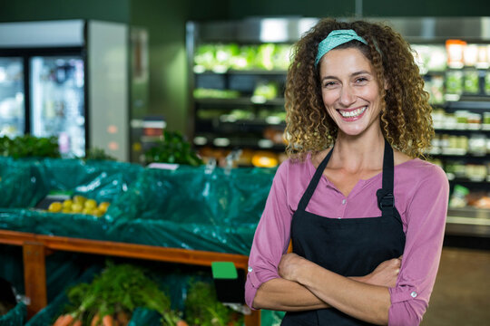Woman wearing pink shirt and apron stocking carrots and lemons in grocery produce aisle, copy space - Powered by Adobe