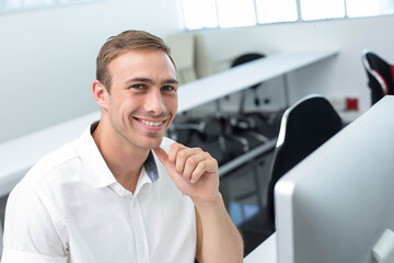 Man smiling and resting hand on chin in computer lab with computer monitor, copy space