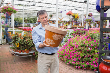 Man inspecting terracotta planter inside greenhouse near potted flowering plants