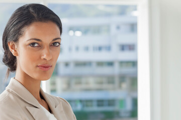 Businesswoman standing near floor-to-ceiling window in office with city skyline view, copy space