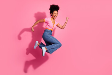 Young woman jumping playfully in casual attire on bright pink background showcasing energy and...