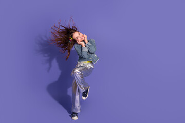 Adorable girl in stylish denim jacket posing vibrantly on a purple backdrop with dynamic hair...