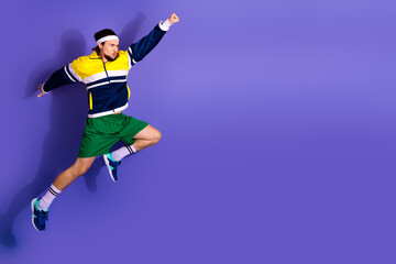 Obraz premium Energetic young man in colorful workout attire jumping against a vibrant purple background, exuding athletic energy