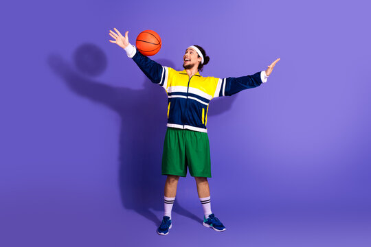 Energetic young man in sporty attire juggling basketball with retro vibes and fun expression against vibrant violet background - Powered by Adobe