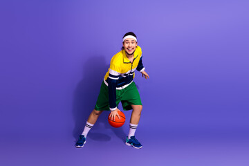 Cheerful athlete in colorful retro sportswear practicing basketball skills on a vibrant purple...