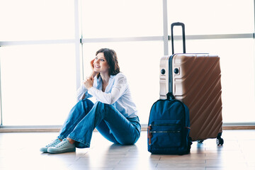Young woman sitting on the floor with luggage at the airport, waiting for her adventure to begin...