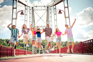 Group of joyful young friends jumping on a bridge during a bright summer day celebrating happiness...