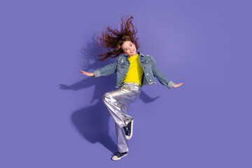 Happy child in a stylish outfit jumping playfully against a vibrant purple background, expressing...
