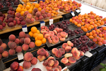 Fresh assorted fruits displayed at a vibrant market stall with colorful peaches, plums, and apricots in abundance