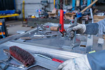 Mains d’un technicien travaillant une pièce métallique sur son établi, avec plusieurs outils disposés en vrac autour de lui dans un atelier.