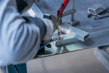 Technicien en train de souder des pièces industrielles métalliques sur son établi dans un atelier de fabrication.