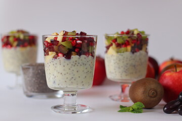 Chia seed pudding or chia custard in glass cups topped with pomegranate, kiwi, apple, and grapes