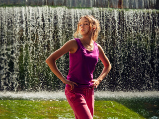 Young fitness girl model is standing in river water with stunning waterfall background. Girl is...