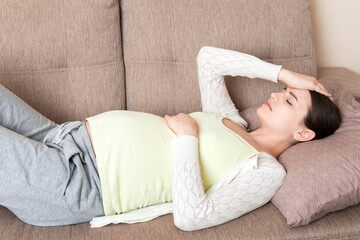 Pregnant woman with painful belly on sofa at home