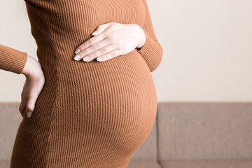 Pregnant woman hold back pain on sofa at thr home Maternity healthcare concept support products.