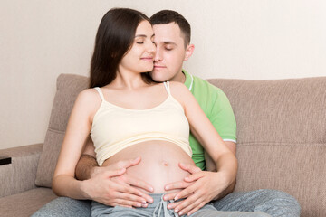 A young couple is expecting a baby. husband hugs the belly of his pregnant wife at home