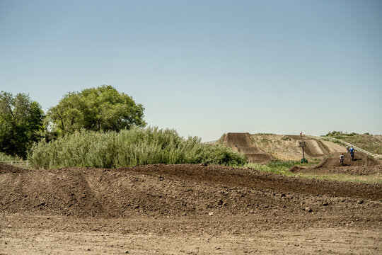 Motocross riders racing on a dirt track with large jumps and blue sky