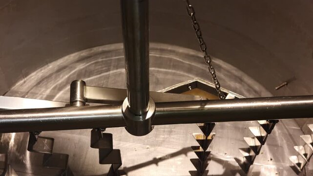 Inside View of Industrial Brewing Mash Tun with Mixer Blades, Close-up footage of an industrial brewing mash tun showing rotating stainless steel mixer blades used in beer production process.
