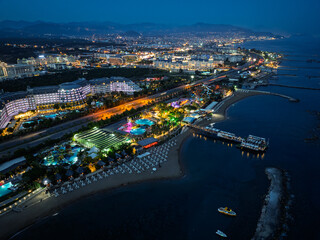 Fototapeta premium Stunning aerial sunset to night transition over Turkler in Alanya, Turkey. Alanya coastline,resorts,marina,hotels and city lights along the Mediterranean Sea drone view. Mediterranean Sea coastline.