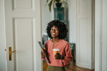 Smiling businesswoman entering home office holding tablet and coffee
