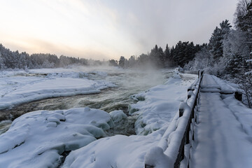Torrent d'eau vive en hiver recouvert partiellement de neige et de glace à côté d'un ponton en...