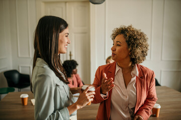 Businesswomen talking and holding takeaway coffee cups during office break