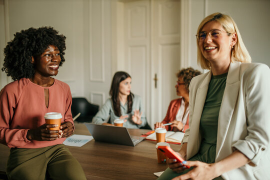Businesswomen having informal meeting, drinking coffee and using mobile phone