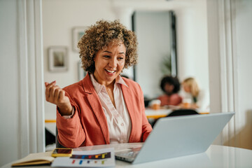 Happy businesswoman working on laptop in modern office with colleagues in background