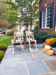 Skeletons sit on chairs in front of the house. Autumn holiday Halloween in America.