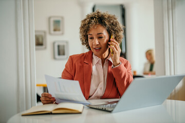 Businesswoman working from home office talking on phone and reviewing documents