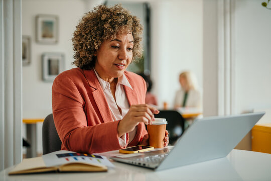 Focused businesswoman working on laptop and drinking coffee in modern office