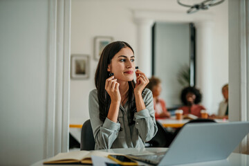 Businesswoman putting on wireless earphones at her desk in the office