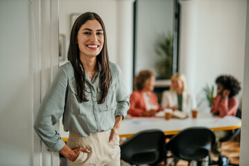 Smiling businesswoman standing at doorway while colleagues are having a meeting