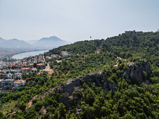 Fototapeta premium Aerial view of turquoise sea with boats near rocky coast and forest in Alanya, Turkey. Summer drone footage of scenic Mediterranean shoreline and clear water. Summer holiday in Alanya.