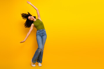 Young stylish woman with curly hair wearing a green top and jeans posing joyfully against a bright...