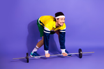Naklejka premium Young male athlete lifting barbell in retro sportswear on vibrant purple background, showcasing fitness and vintage style