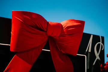 Large red bow decorates a gift box against a clear blue sky during a festive celebration