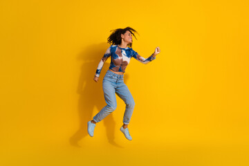 Energetic young woman jumps joyfully against a vibrant yellow background showcasing casual style...