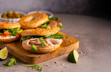 Variety of Bagel sandwiches with ricotta, prosciutto or chicken ham or salmon and microgreens, bagel with ham for breakfast on gray background, close up. Healthy breakfast food.