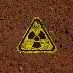 Yellow radioactive sign on brown ground, top view. Radiological pollution